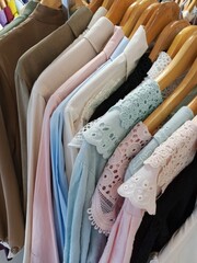 A neat rack of blouses and shirts in soft pastel colors, showcasing delicate lace and textured fabrics on wooden hangers