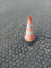 A solitary, weathered orange and white traffic cone stands on a patterned, hexagonal pavement, with...