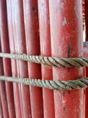 A close-up of thick, worn rope tied around a series of faded, peeling red metal poles