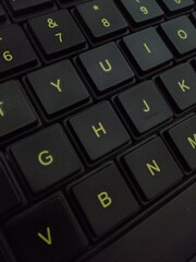 A close-up, angled view of a black computer keyboard, showing the keys with glowing, yellowish-green lettering