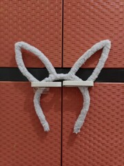 A close-up of a pair of plush, gray bunny ears hanging on the handles of a textured, reddish-brown cabinet