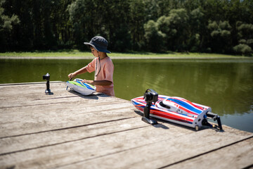 Child preparing toy rc boat for racing on wooden pier