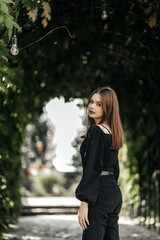 A girl in a park on a summer day, dressed in black, looking straight into the camera.