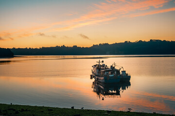 Two lone fishing boats floating on calm waters as the sun rises over Castro, Chilo? island, Chile. Fishing and sea farming activities are important economic sources in the Chilo? archipelago.