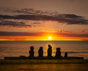 Silhouettes of the five restored moai statues at Ahu Vai Uri, Rapa Nui (Easter Island), Chile, against the beautiful glow of the sun setting over the Pacific Ocean. The ahu dates back to 1200 AD.