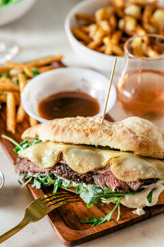Close-up of French dip sandwich with au jus, fries, and wine.