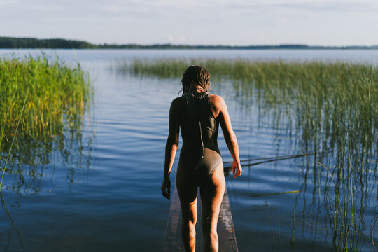 Woman walking on a wooden dock by the lake, surrounded by tall reeds
