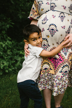 Latino son hugs moms pregnant belly outside in green nature