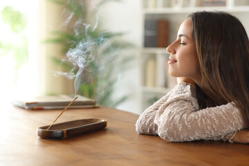 Happy woman smelling burning incense relaxing at home