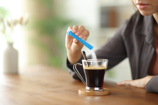 Woman hand throwing sugar in a coffee cup on a table at home