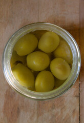 Green olives in a glass jar on a wooden cutting board
