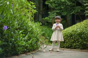 happy toddler girl in white dress with Ruellia simplex or Mexican petunia flower in garden