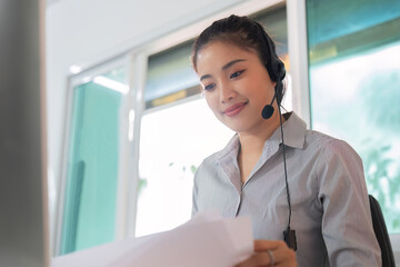 Virtual Communication. Focused woman reviewing documents while on a headset in a modern workspace.