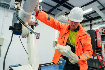 Asian male automation specialist testing robotic machinery in industry 4.0 lab wearing safety gear...