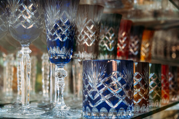 Colorful cut crystal glassware arranged on a shelf in a store display. Craftsmanship, artisanal glassmaking, decorative objects, luxury homeware