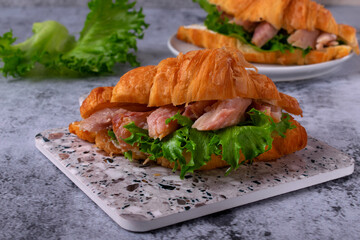 Croissant sandwich with pieces of hot smoked fish catfish clarias on grey table