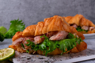 Croissant sandwich with pieces of hot smoked fish catfish clarias on grey table
