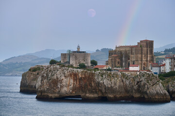 rainbow, moon and santa maria de la asuncion church rising over castro urdiales, spain