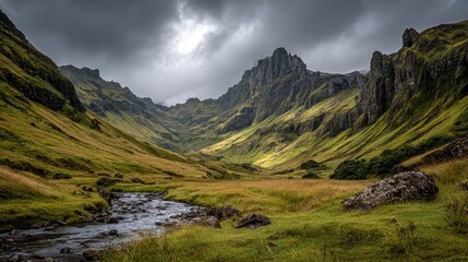 Naklejka premium Sunlit valley with a stream, dramatic mountains and cloudy sky