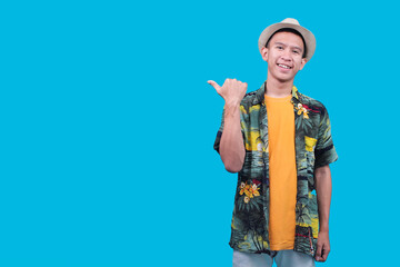 Happy Young Asian Man Smiling And Pointing His Thumb To The Empty Space On A Blue Background