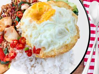 Stir-fried squid with basil and fried egg on rice, on the white plate, with spoons, fork, cloth,...