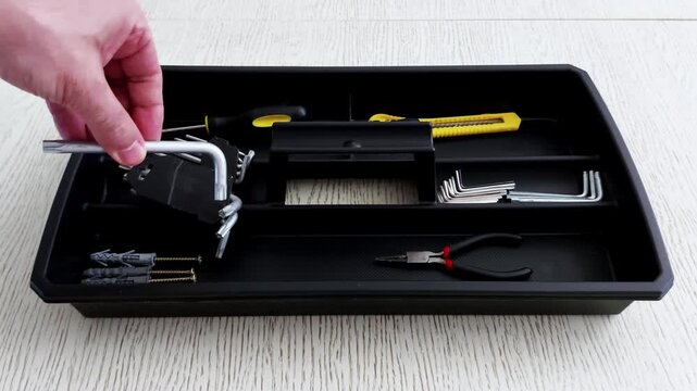 A hand places a metal clamp into a black tool tray-surrounded by hex keys, cutters, and screws. A quiet moment of setup, precision, and workspace rhythm