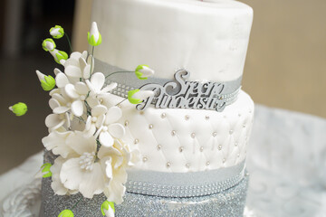 A whole three-tiered white cake decorated with edible flowers. On a waiter's cart, ready for...