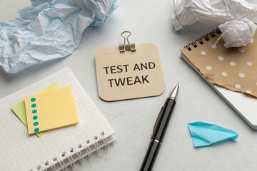 Workspace with crumpled papers, sticky notes, and a notepad showcasing a test and tweak message