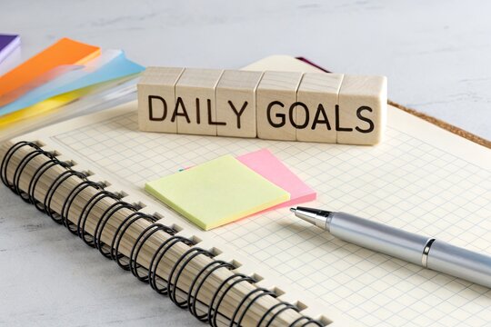 Organized workspace with sticky notes and wooden blocks spelling 'DAILY GOALS' for productivity