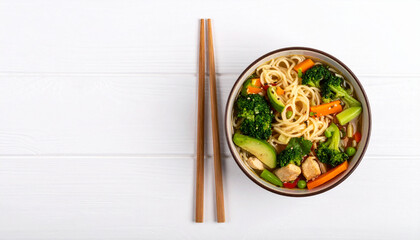 Healthy vegetarian noodle soup with chopped herbs floating in clear broth served in bowl with wooden chopsticks on white wooden table, fresh and colorful meal