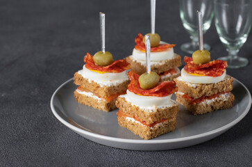 Canapes with salami, egg, olives and kimchi on gray plate
