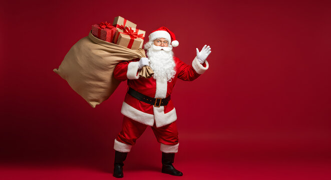 Happy old funny Santa Claus, Saint Nicholas wearing costume holding sack bag with Merry Christmas presents walking delivering xmas gifts standing isolated on red background. Xmas delivery, banner. - Powered by Adobe