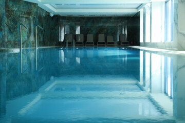 Luxury indoor swimming pool with clear blue water and empty lounge chairs, modern spa and wellness...