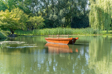 Boat on the pond. A traditional wooden boat floats serenely on a green pond, surrounded by reeds...