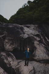 Young man standing on rocky terrain near water.