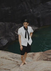Young man in fashionable attire near water on rocks.