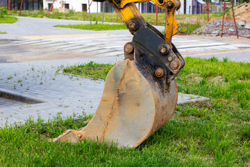 A bright yellow excavator bucket is resting on the green grass