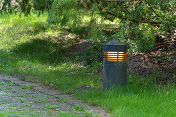 Garden light by the path. A black garden light shines along the edge of a path paved with natural...
