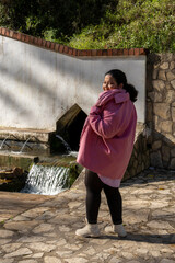 A woman in a pink coat stands in front of a stone wall