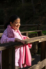 A woman in a pink shirt and scarf stands on a wooden bridge