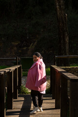 A woman in a pink coat stands on a wooden bridge