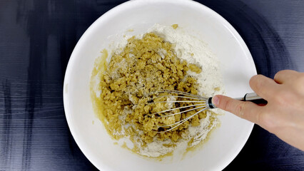 Mixing flour with melted butter in white bowl using whisk, hand stirring ingredients on black...