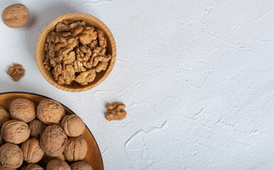 Shelled walnuts lie in two wooden bowls on a textured white table with space for an inscription.