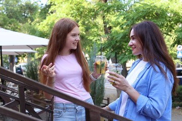 Beautiful mother and her teenage daughter with refreshing drinks talking on stairs outdoors