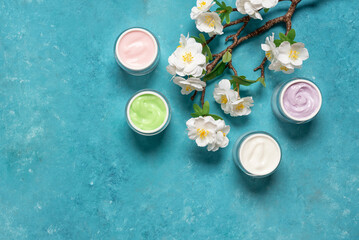 Set of different cosmetic creams with decorative flowering cherry branch on blue grunge background,...