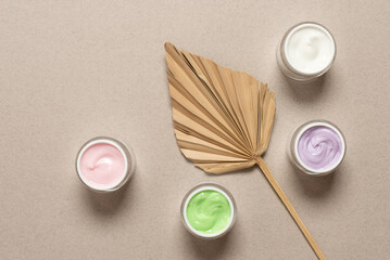 Set of cosmetic creams of different colors on beige background decorated with palm leaf fan, top...