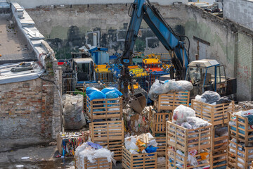 Waste recycling plant with grab arm. A grab arm lifts garbage and recycling material in a yard....