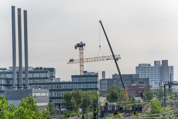 A crane raises a boom arm over modern office and industrial buildings. The scene depicts urban...