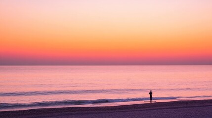 Fototapeta premium Silhouetted figure on a beach at sunset. Peaceful ocean panorama. Soft colors of sunrise
