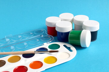 There are jars of gouache paints on a blue background.